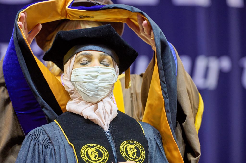 A UNC Greensboro School of Nursing doctoral student getting hooded at graduation.