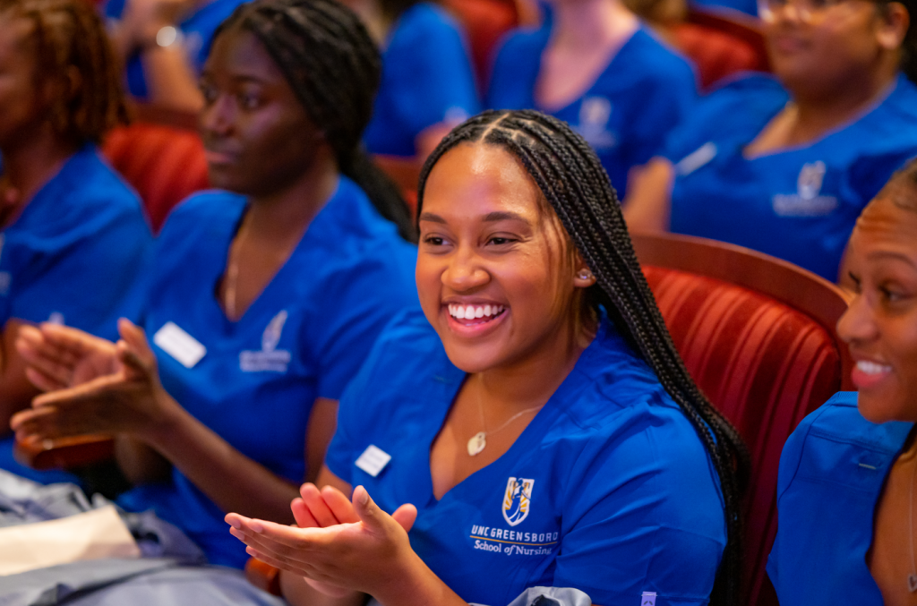 A UNC Greensboro School of Nursing student smiles and claps at the Coating Ceremony.