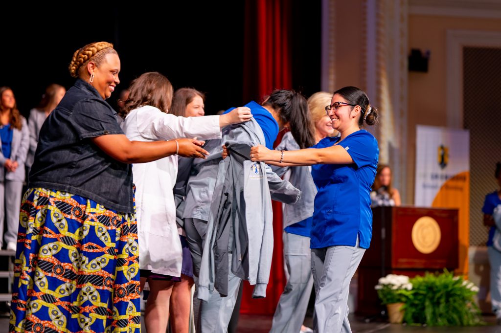 A UNC Greensboro School of Nursing presents a coat to a staff member at the Coating Ceremony.