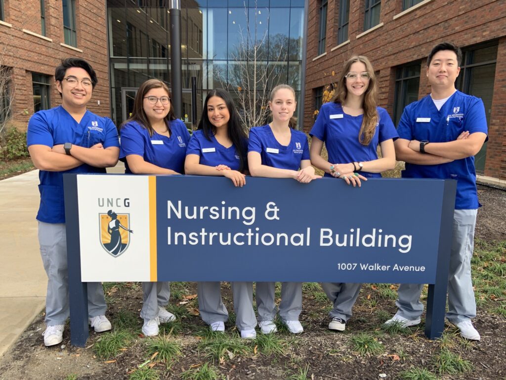 UNCG School of Nursing BSN students standing by the Nursing and Instructional Building sign.
